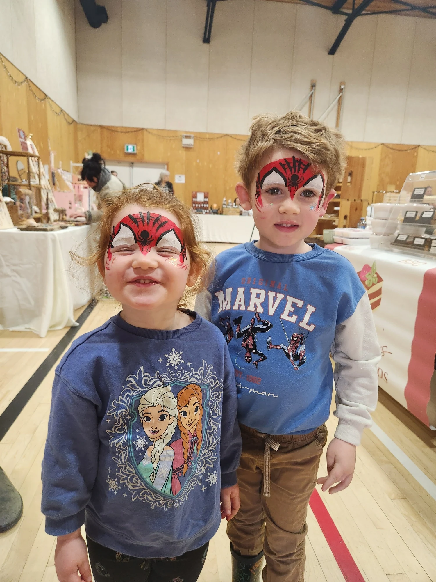 Two young children with red and black Spider-Man face painting at an event