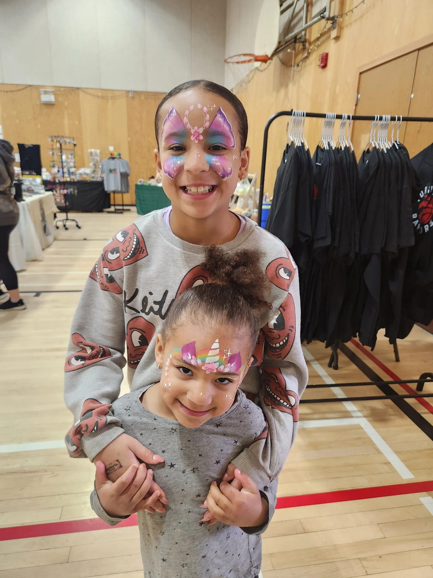 Two children with unicorn and butterfly face painting designs at a market