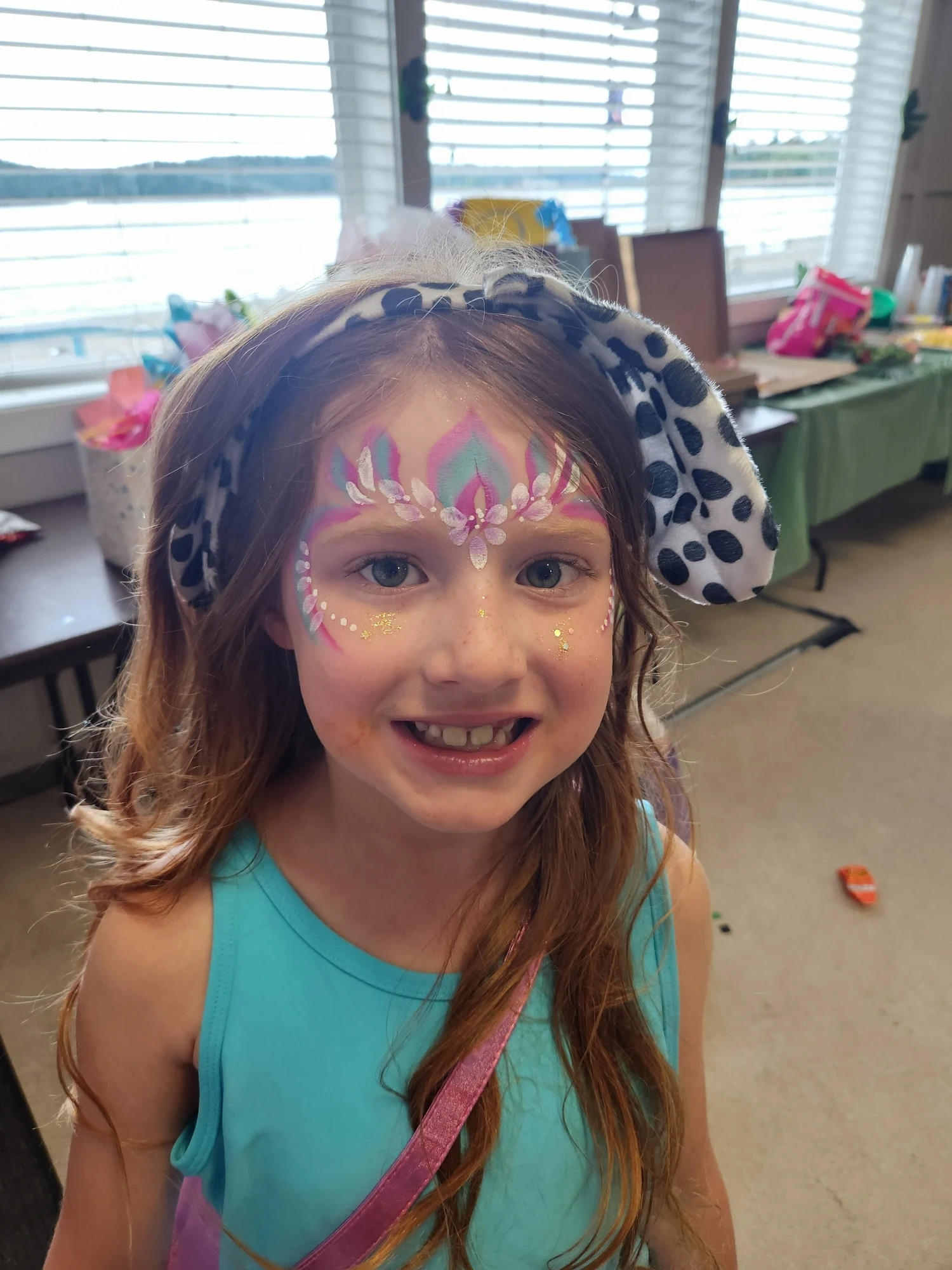 Young girl with a pink and teal princess crown face painting and glitter, wearing dalmatian ears